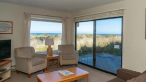 A room with a TV, two armchairs, a coffee table, and a large window with a view of the beach. - 2nd floor, panoramic views, 2-person soaking tub, fireplace (Moss Landing)