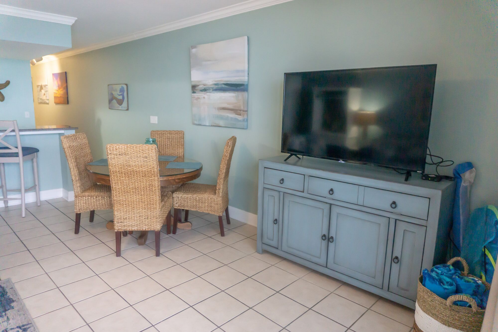 A dining area with wicker chairs and a round table, a television on a cabinet, and artwork on the wall.