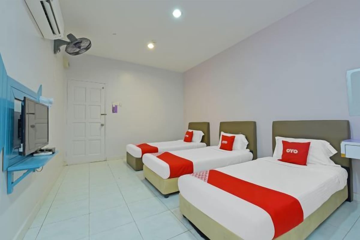 Habitación de hotel con tres camas, televisión y ventilador de techo.