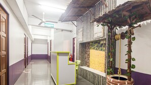A hallway with a reception desk, a fire extinguisher, and a decorative planter with a rope and a small tree. - Hotel O Purple Town (Sekinchan)