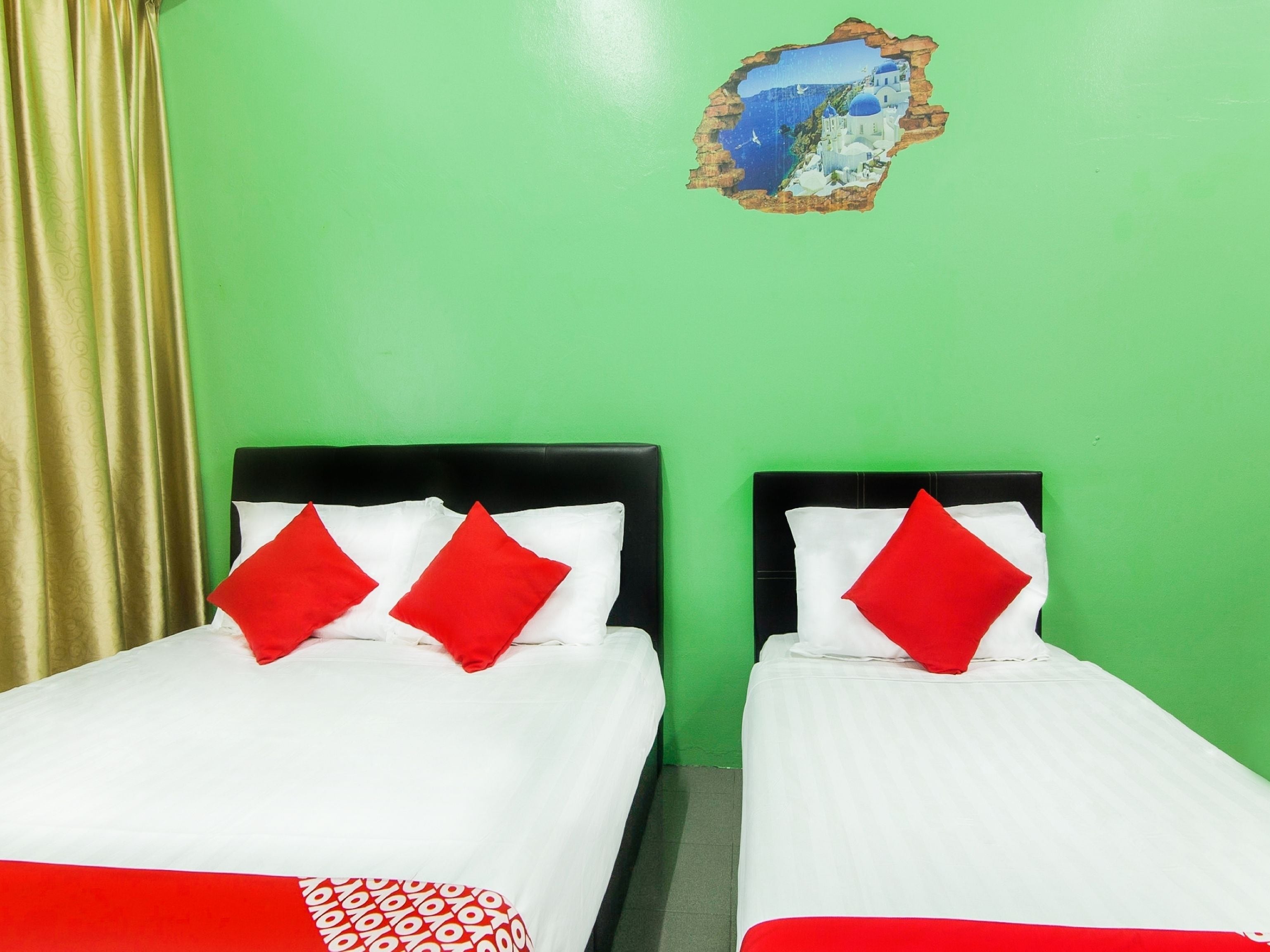 A room with two beds, each with white bedding and red pillows, against a green wall.