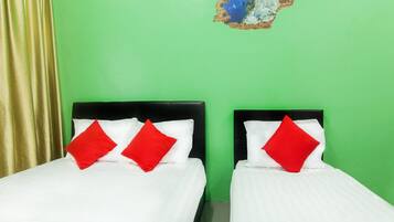 A room with two beds, each with white bedding and red pillows, against a green wall.
