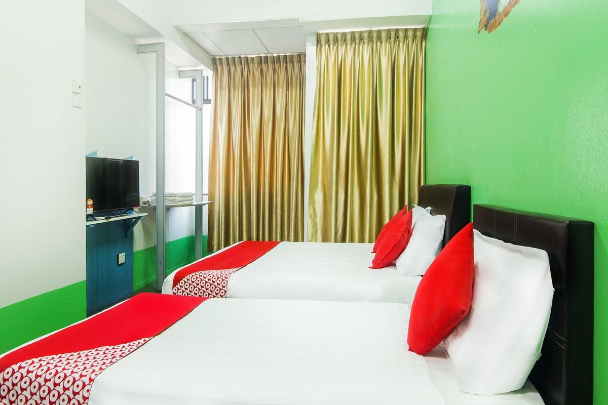 Une chambre d’hôtel avec deux lits, une télévision et un mur vert.