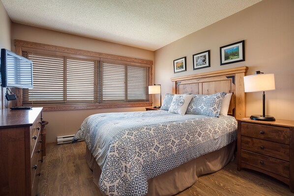 A bedroom with a bed, bedside lamps, a desk with a computer, and a window with blinds.