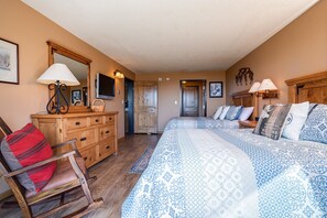 A bedroom with a large bed, a wooden dresser, a chair, and a television on the wall.