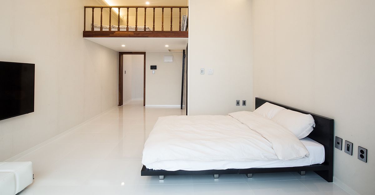 A modern bedroom with a large bed, a TV mounted on the wall, and a staircase leading to an upper level.