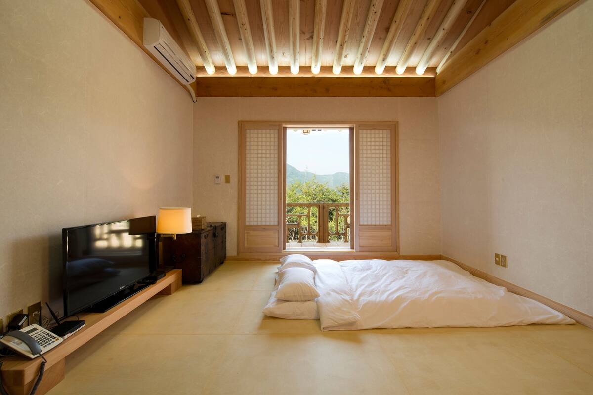 A room with a TV, bedside lamp, and a bed with pillows.