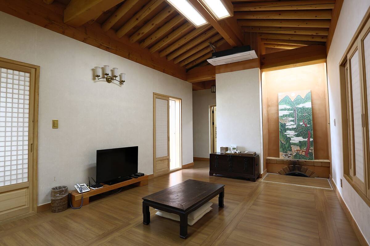 A traditional Japanese room with wooden flooring, a television, a small table, and a painting of a waterfall.