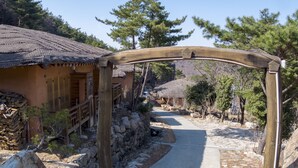 A traditional wooden gate leading to a pathway flanked by stone walls and wooden structures. - Hotel de forRe (Daegu)