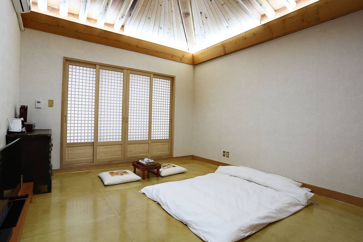 A room with a large shoji screen door, a bed with white bedding, a small wooden table, and a desk with a computer and other items.