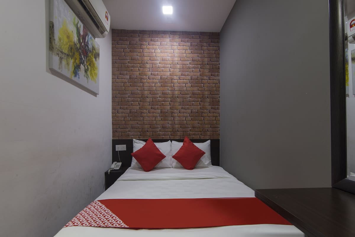 Une chambre d’hôtel avec un mur d’accent en briques, un lit avec une literie blanche et des oreillers rouges, une table de chevet et une petite table de nuit avec un téléphone.
