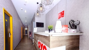 A hotel reception area with a wooden reception desk, a potted plant, a fan, and a sign indicating a 2 PM checkout. - OYO 876 Hotel Sanctuary (Petaling Jaya)