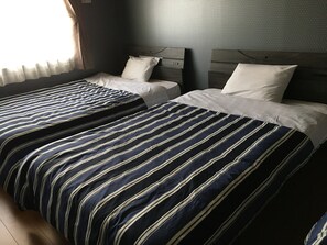 A hotel room with two beds, each with striped bedding and white pillows. - Beppu Hostel U&T (Beppu)