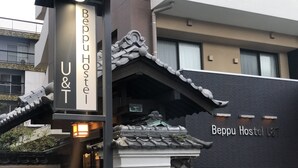 Il s'agit d'une auberge de jeunesse au style architectural japonais traditionnel, caractérisée par un toit en tuiles et une base en pierre. Le nom de l'auberge, « Beppu Hostel », est affiché en grand sur une enseigne.