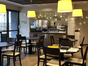 Un café con mesas y sillas, un letrero de zona para fumadores, una máquina de Pepsi y un anuncio de bebida gratis.