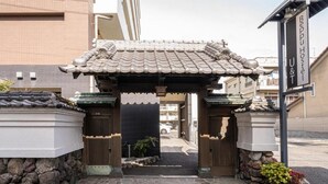 Une porte d’entrée traditionnelle japonaise, surmontée d’un toit en tuiles, mène à un bâtiment sur lequel on peut lire l’inscription « Bepu Hostel U&T ».