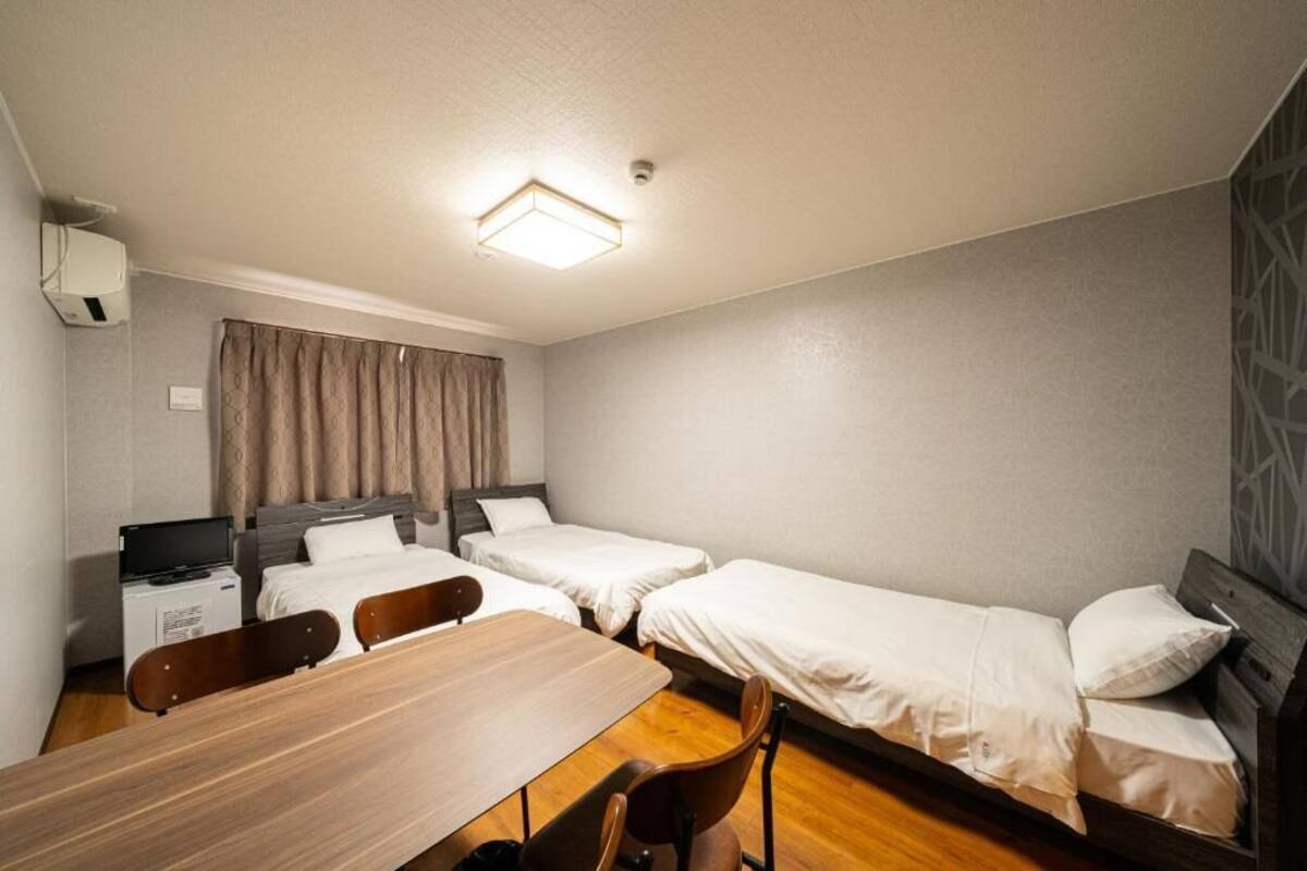 A hotel room with a wooden desk, two single beds, a TV, and a ceiling light.