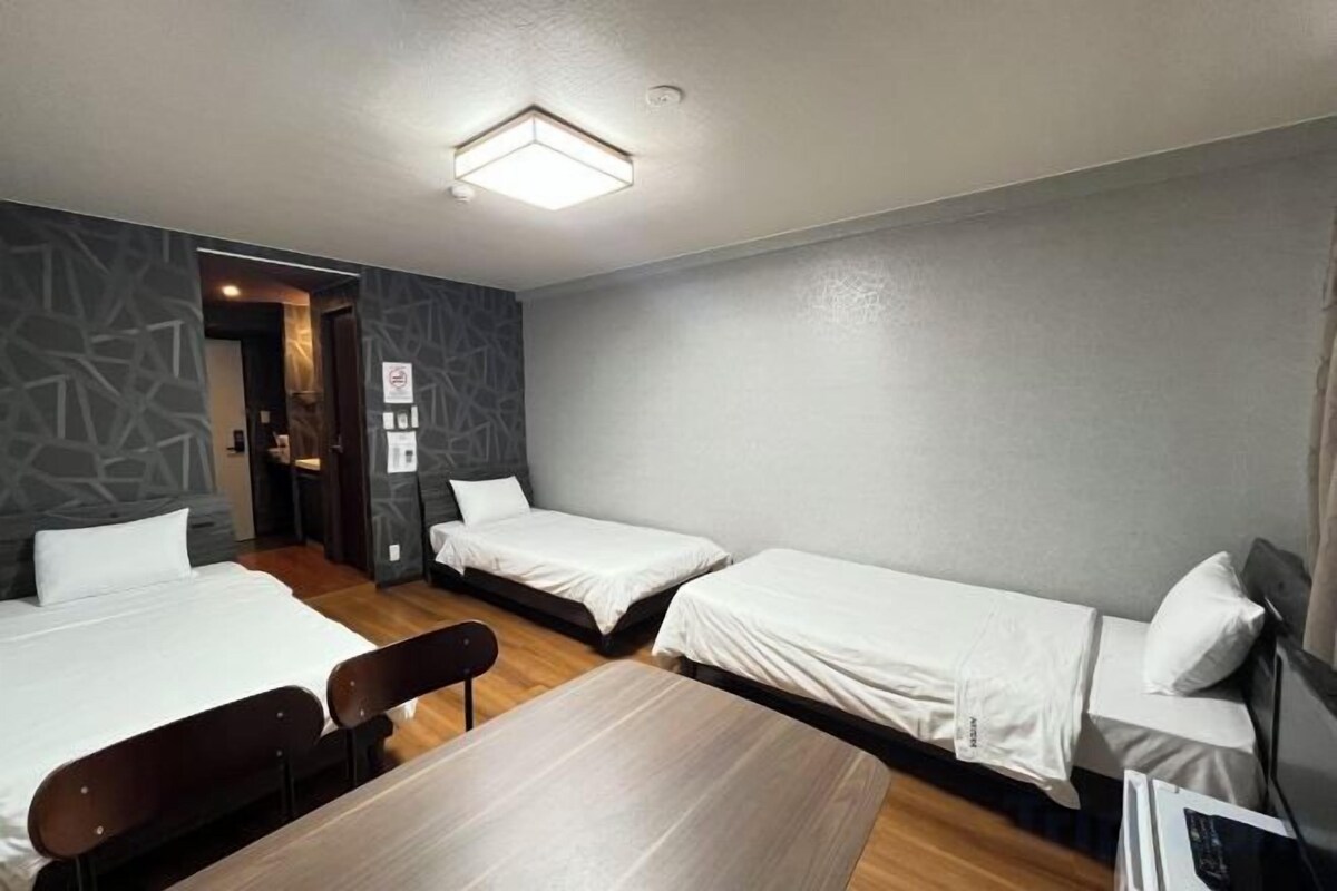 Een hotelkamer met drie eenpersoonsbedden, een houten tafel en een stoel.