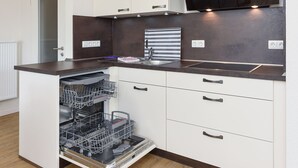A modern kitchen with white cabinetry, a dark countertop, and a built-in dishwasher. - Vacation apartment top right - Haus Fallen Anker in Neuharlingersiel (Neuharlingersiel)