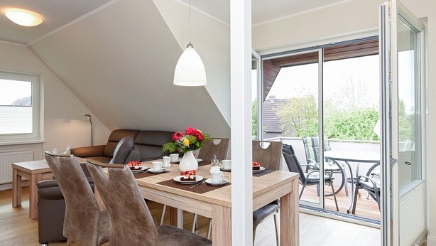 A dining area with a wooden table, chairs, and a vase of flowers. - Vacation apartment top right - Haus Fallen Anker in Neuharlingersiel (Neuharlingersiel)
