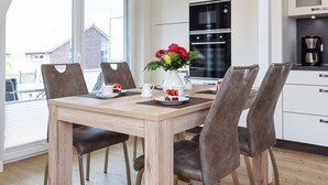 A modern kitchen with a dining table, chairs, and a hanging light fixture. - Vacation apartment top right - Haus Fallen Anker in Neuharlingersiel (Neuharlingersiel)