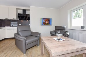 Ett modernt kök med vita skåp, en grå soffa och ett matbord i trä.
