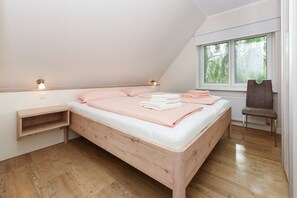 Un dormitorio con una cama de madera, una mesita de noche, una silla y un ventanal con vistas a árboles.