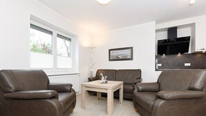 A modern living room with two brown leather sofas, a wooden coffee table, and a large window providing natural light.