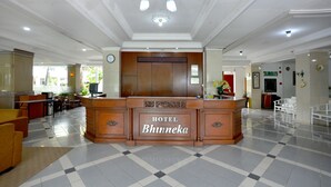 A hotel reception area with a check-in counter, a clock, and a view of the outdoor seating area.