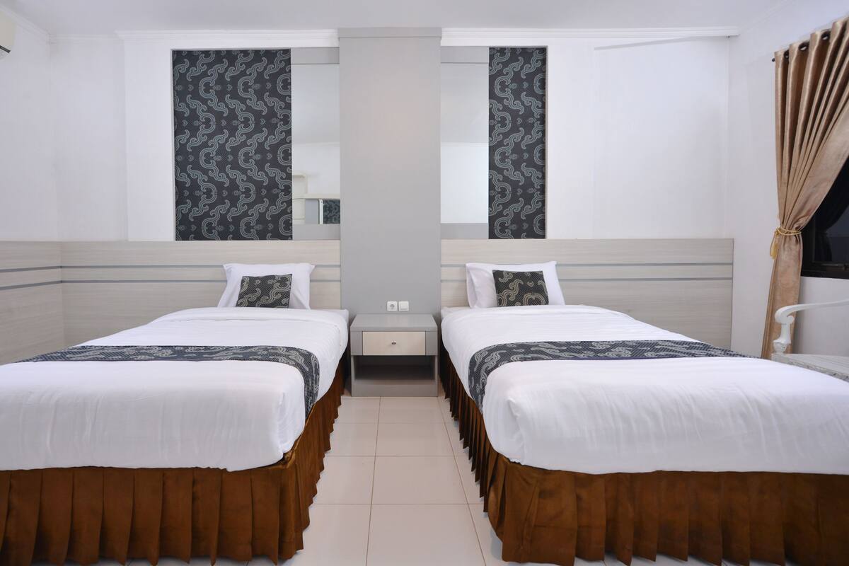 Una habitación de hotel con dos camas individuales, una mesita de noche y un espejo.