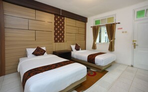 Habitación de hotel con dos camas individuales, cabecero de madera, un escritorio pequeño, ventana con cortinas y una puerta.
