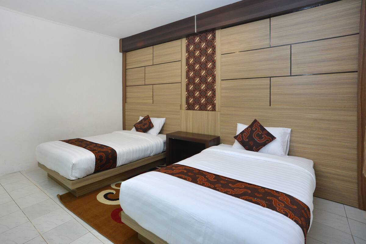Habitación de hotel con dos camas individuales, cabecera de madera, pared decorativa con estampado y alfombra marrón.