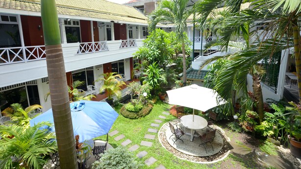 A courtyard with a dining area, palm trees, and a building with a tiled roof.