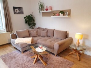 A modern living room with a beige sectional sofa, a glass coffee table, a small round table with a lamp, and a potted plant.