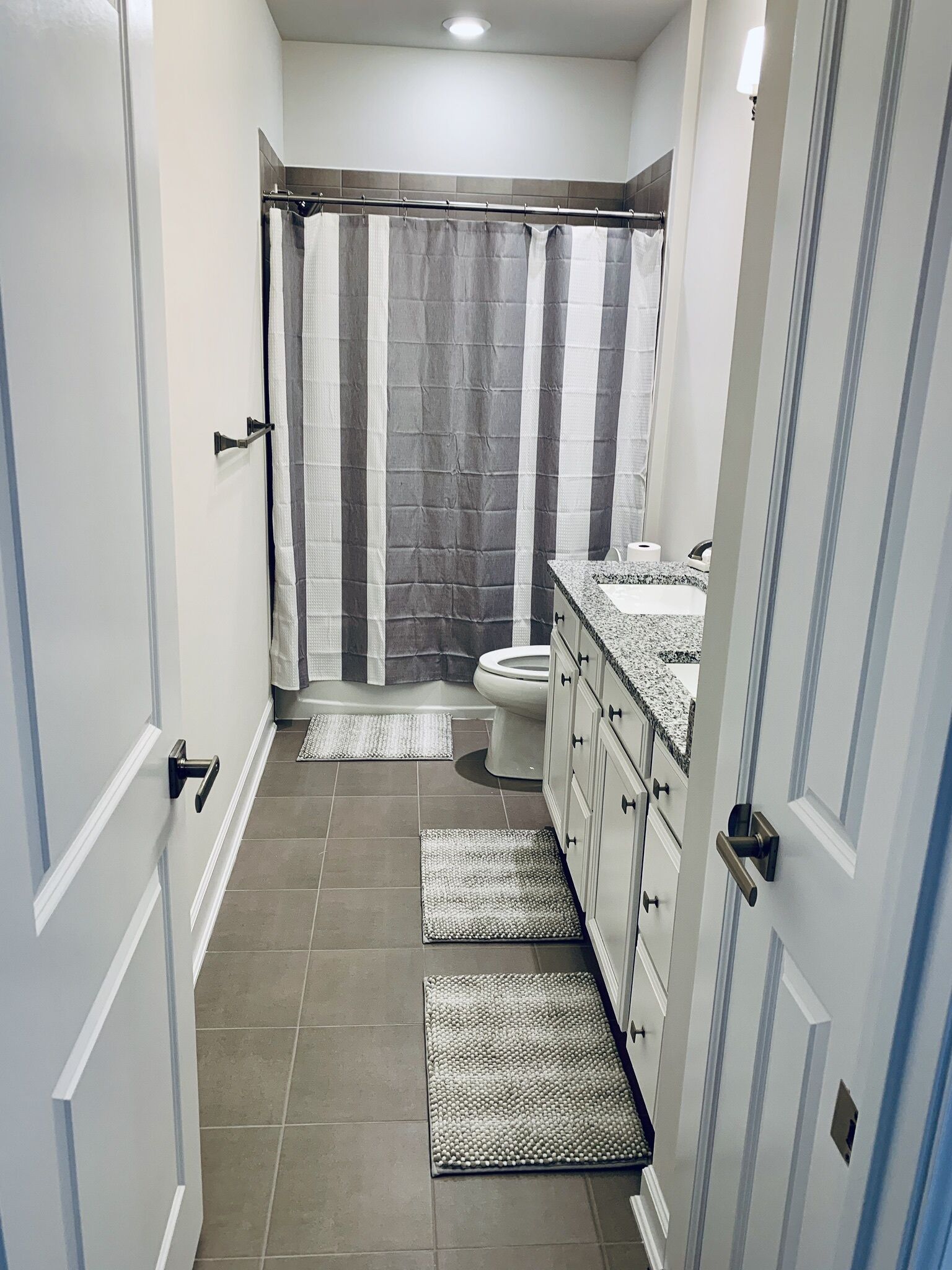 A narrow bathroom with a shower, toilet, and sink.