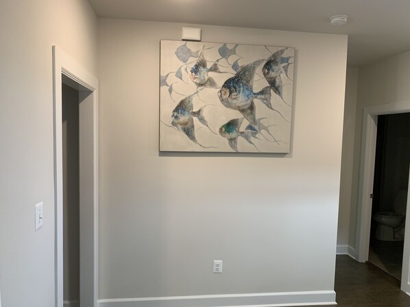 Un couloir avec un mur blanc et un tableau abstrait représentant des poissons, encadré.