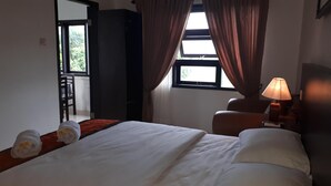 Une chambre d’hôtel avec un lit, un bureau, une chaise, une lampe et une fenêtre avec des rideaux.