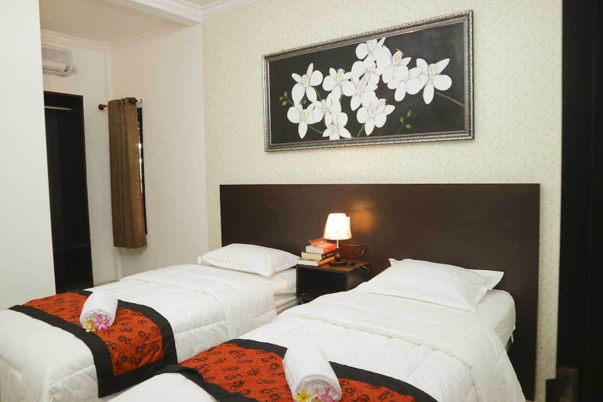A hotel room with two beds, a nightstand with a lamp, a framed floral artwork on the wall, and a door with a curtain.