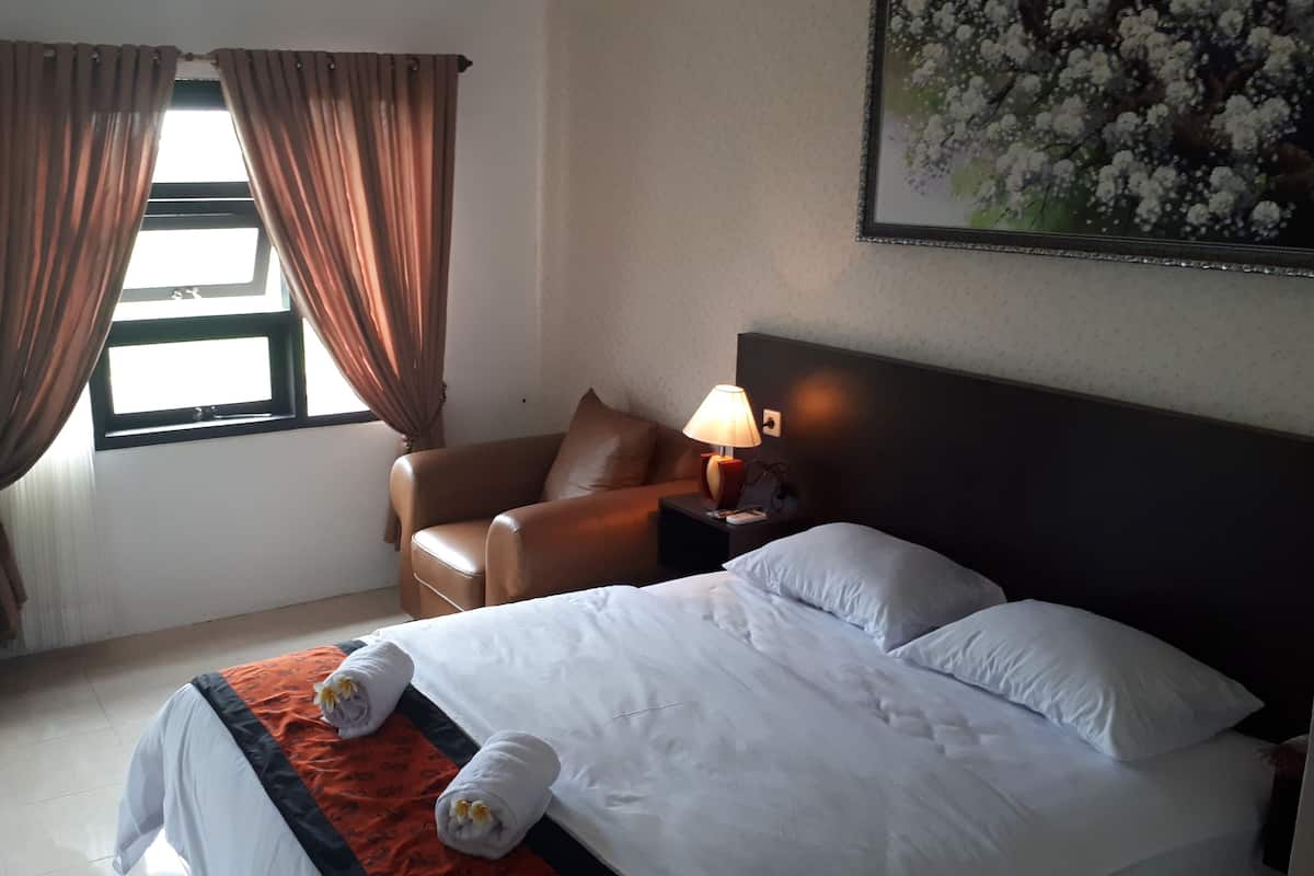 A hotel room with a bed, a chair, a nightstand with a lamp, and a window with curtains.