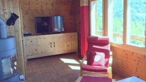 A cozy cabin room with a wooden interior, a television on a cabinet, a red chair, and a window with a view of greenery. - Outside : 2-storey flat in a typical chalet in Chandolin, for 5 persons, beautiful terrace with nice (Chandolin)