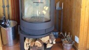 A wood-burning stove with a glass door, logs in front, and a metal pot to the left. - Outside : 2-storey flat in a typical chalet in Chandolin, for 5 persons, beautiful terrace with nice (Chandolin)