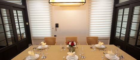 Mesa de comedor preparada para cuatro personas, con platos blancos, detalles dorados y un arreglo floral en el centro.