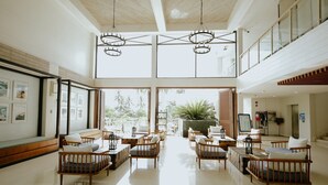 A spacious lobby with high ceilings, wooden furniture, and large windows offering views of greenery. - Club Samal Resorts Development Inc (Samal)