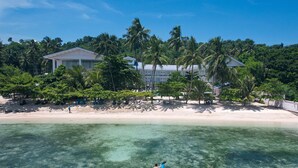 A beach with clear water, a person kayaking, and a large building surrounded by palm trees. - Club Samal Resorts Development Inc (Samal)