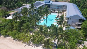 A resort with a large pool surrounded by palm trees, a beach, and a modern building with a blue roof. - Club Samal Resorts Development Inc (Samal)