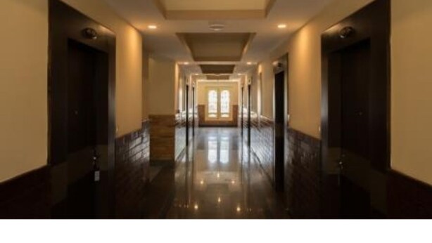 A long, narrow hallway with dark flooring and light walls, leading to a bright room with large windows. - Hotel Lhayul (Ha)