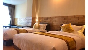 A hotel room with three beds, a brick accent wall, and a large window with curtains. - Hotel Lhayul (Ha)