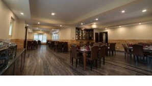 A spacious dining area with multiple tables and chairs, a bar area, and a view of the adjacent room. - Hotel Lhayul (Ha)
