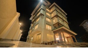 A multi-story hotel with a central courtyard, balconies on each floor, and a well-lit entrance. - Hotel Lhayul (Ha)