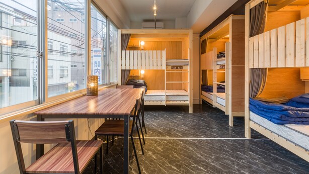 A compact room with a wooden table and chairs, a bunk bed, and a small desk area. - The Aquarius Inn - Hostel (Fukuoka)